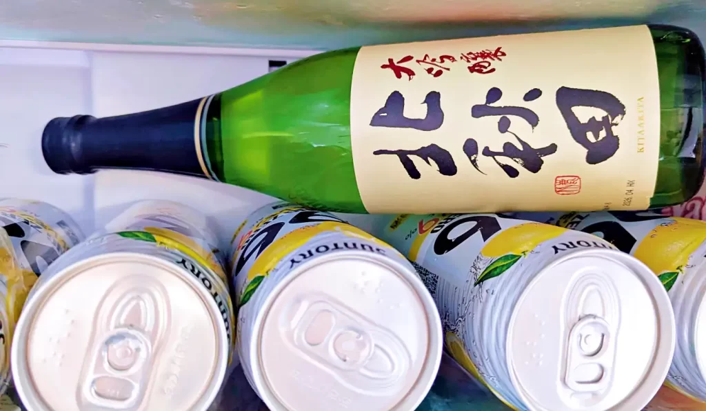 冷蔵庫の棚に横置きされた日本酒「大吟醸 北秋田」の一升瓶。周囲にはレモンサワー缶が並び、晩酌用にしっかり冷やされている様子が分かる。白いラベルに大きく描かれた「北秋田」の筆文字が印象的な日本酒の保管風景。